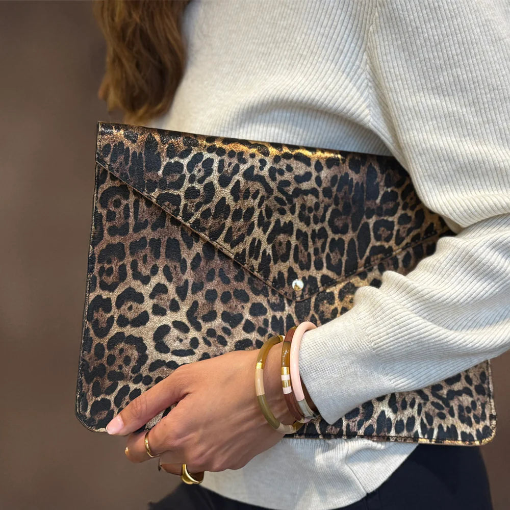 Person holding a leopard print clutch bag with a blurred background