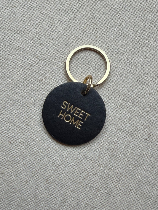 Black keychain with 'SWEET HOME' text on a gray fabric background