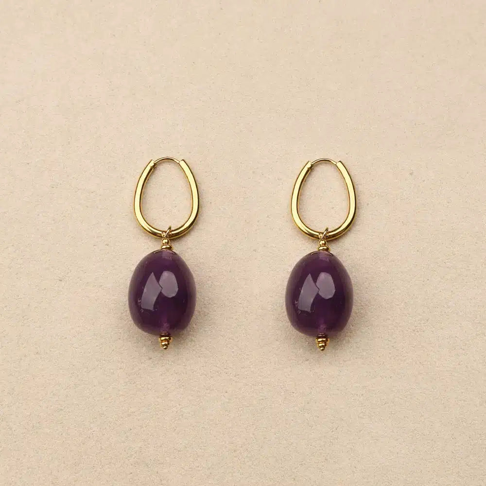 Pair of gold hoop earrings with purple beads on a beige background