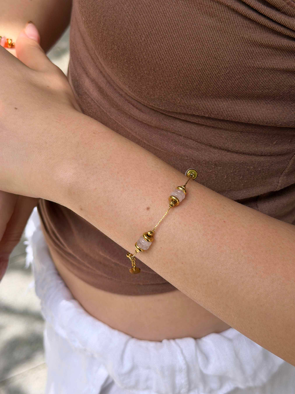 A delicate gold chain bracelet with small gold beads and translucent white stone accents worn on a person's wrist, shown in a close-up lifestyle shot.
