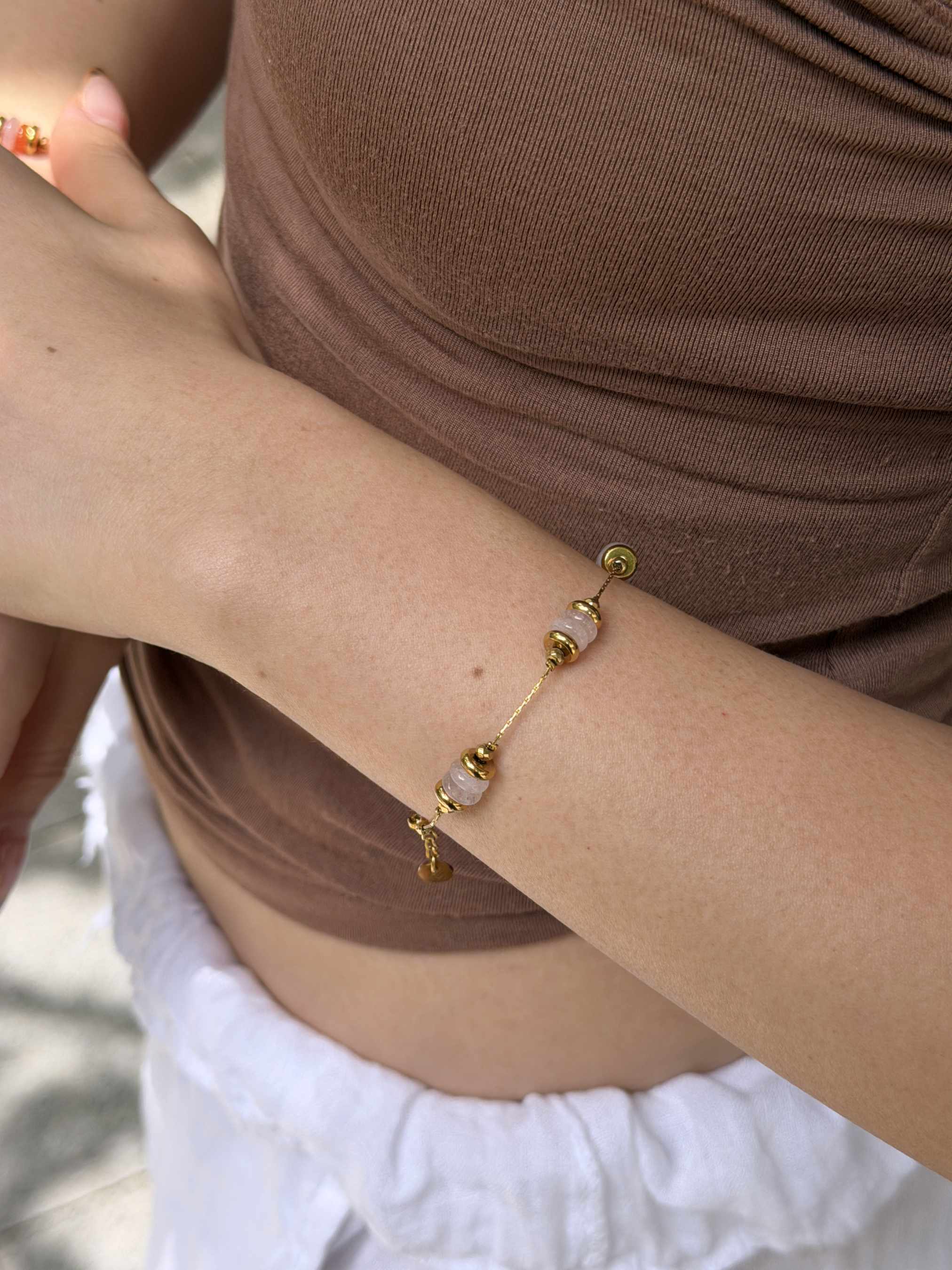 A delicate gold chain bracelet with small gold beads and translucent white stone accents worn on a person's wrist, shown in a close-up lifestyle shot.