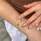 A close-up of a person's wrist and hand wearing a delicate gold chain bracelet with white and gold beads, styled with manicured nails.