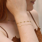 Close-up of a person wearing Khaki gold bracelets on a neutral background