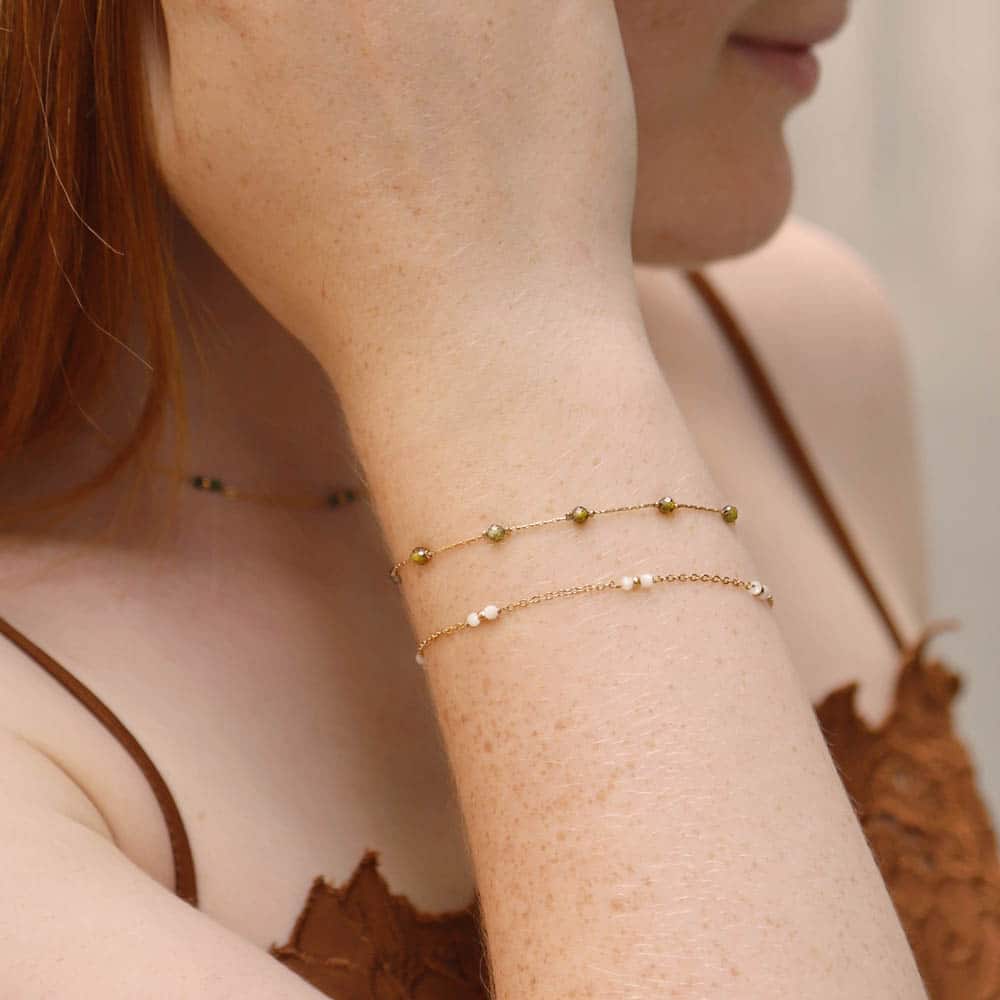 Close-up of a person wearing Khaki gold bracelets on a neutral background