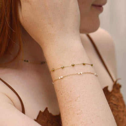 Close-up of a person wearing Khaki gold bracelets on a neutral background