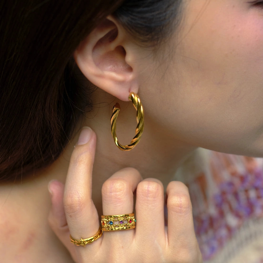 Close-up of a person wearing gold hoop earrings and rings.