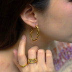 Close-up of a person wearing gold hoop earrings and rings.