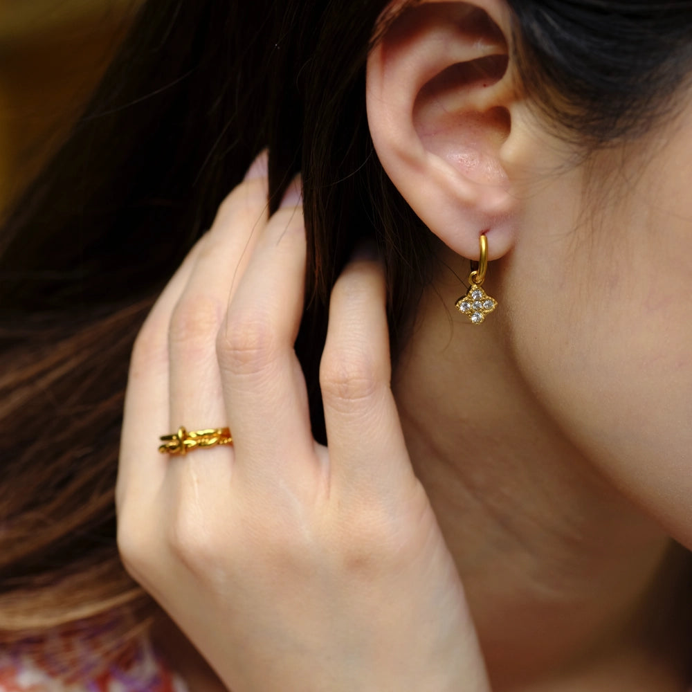 Close-up of a person wearing gold earrings and a ring, with a blurred background.