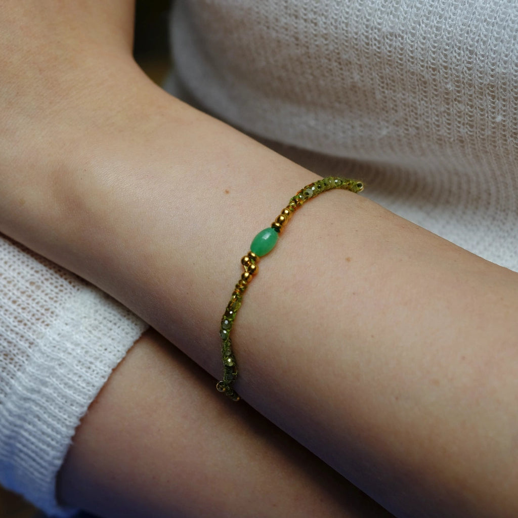 Gold bracelet with a green bead on a wrist against a white sleeve.