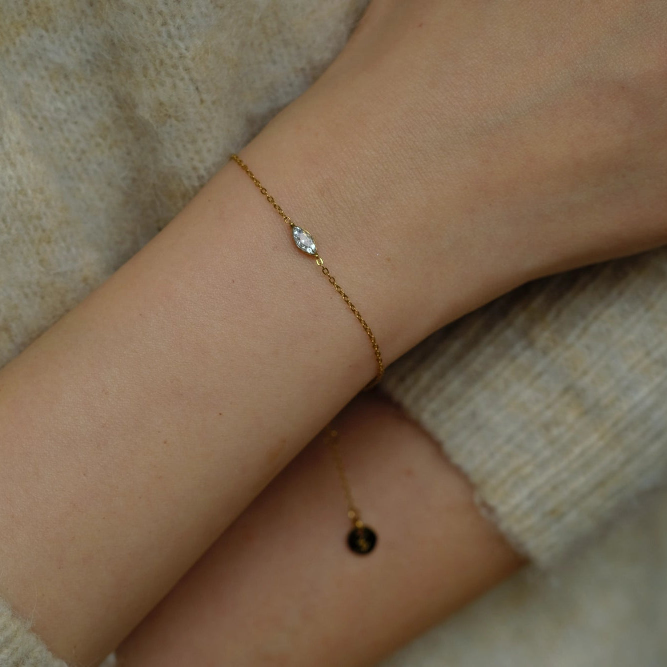 Gold bracelet with a small diamond on a person's wrist against a neutral background