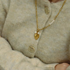Close-up of a person wearing a beige sweater with a gold necklace and heart-shaped pendant.
