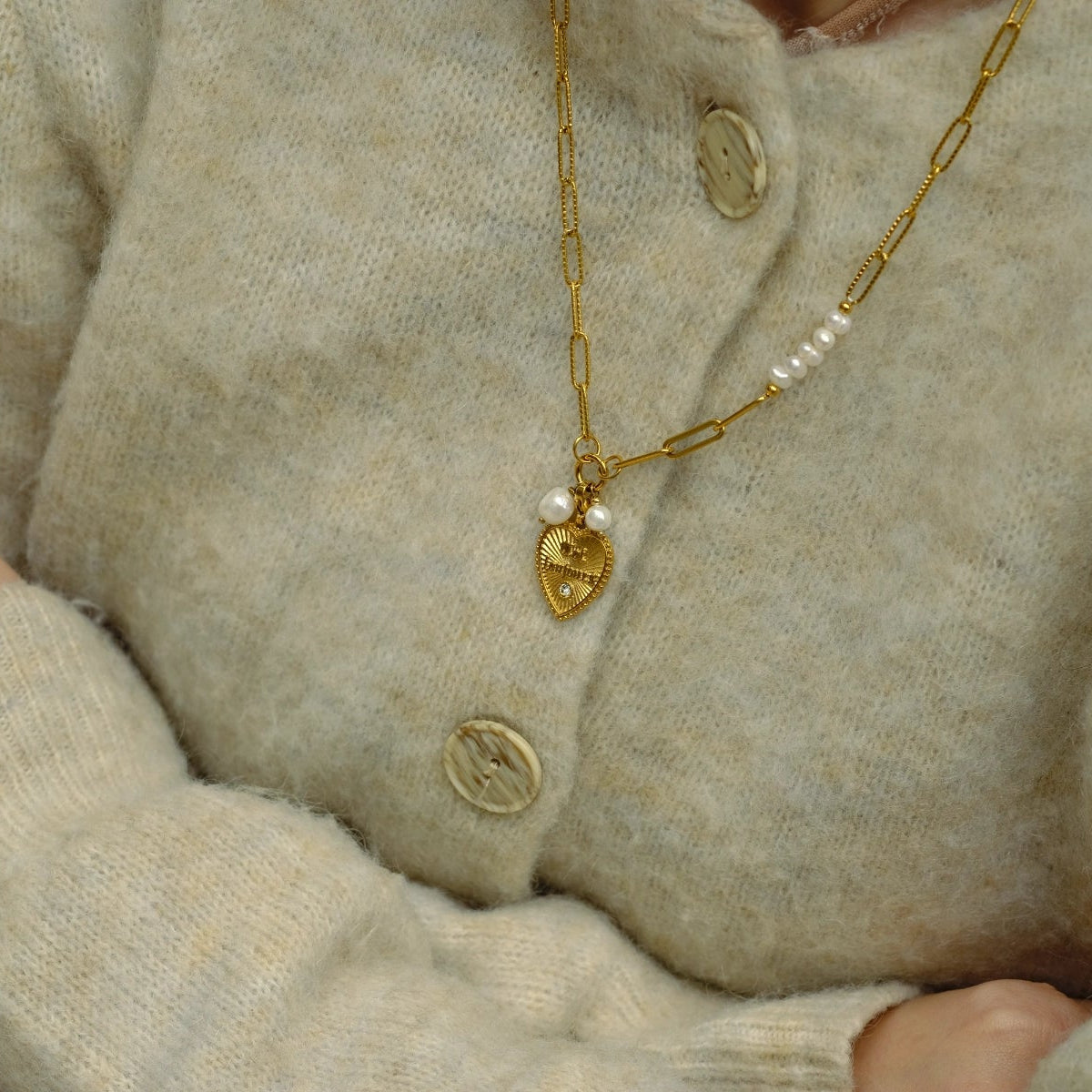 Close-up of a person wearing a beige sweater with a gold necklace and heart-shaped pendant.
