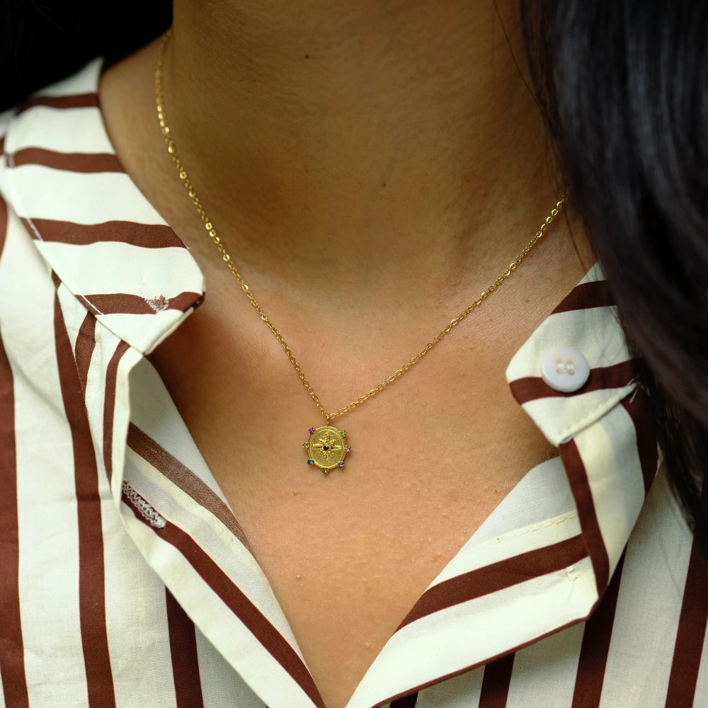 Close-up of a person wearing a gold necklace with a heart pendant, against a blurred background.