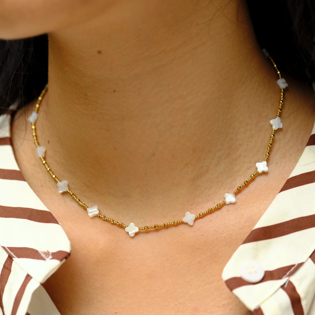 Gold necklace with small white beads worn by a person with striped clothing.