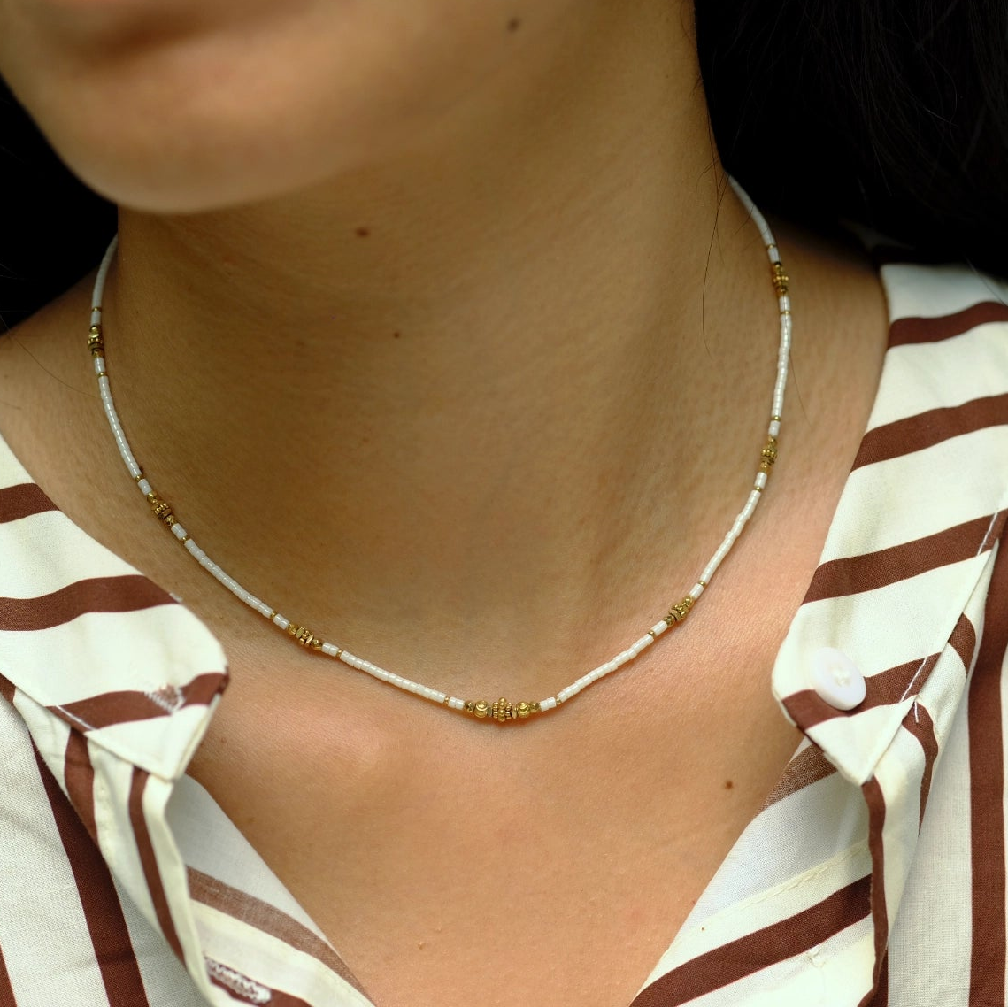 Close-up of a person wearing a gold necklace with a striped shirt.