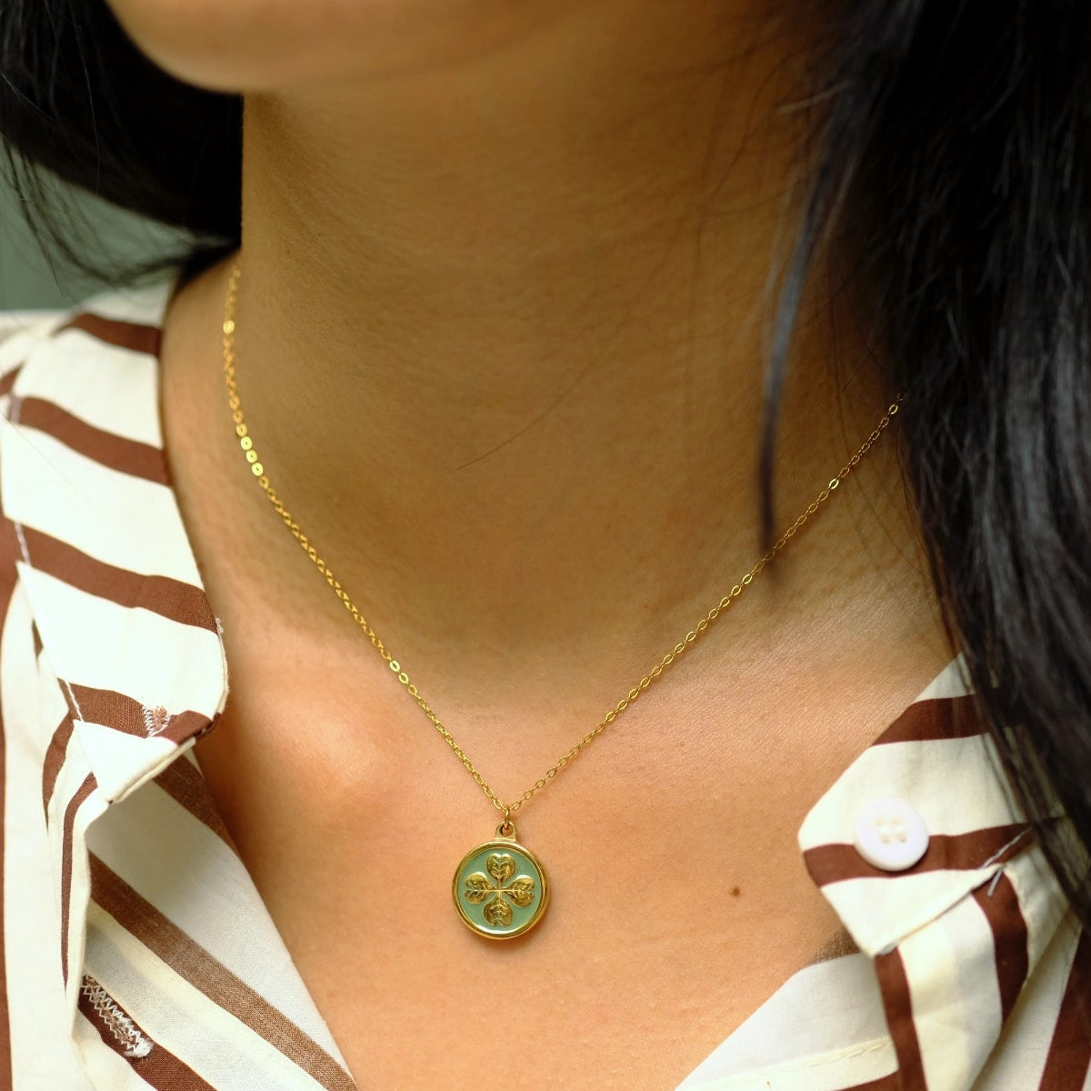 Close-up of a person wearing a gold necklace with a green pendant.
