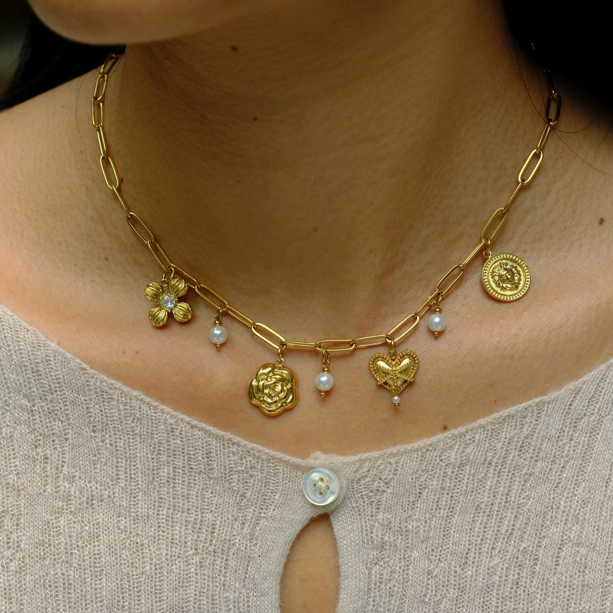 Gold necklace with heart and flower pendants on a person wearing a light gray top.