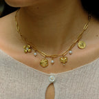 Gold necklace with heart and flower pendants on a person wearing a light gray top.