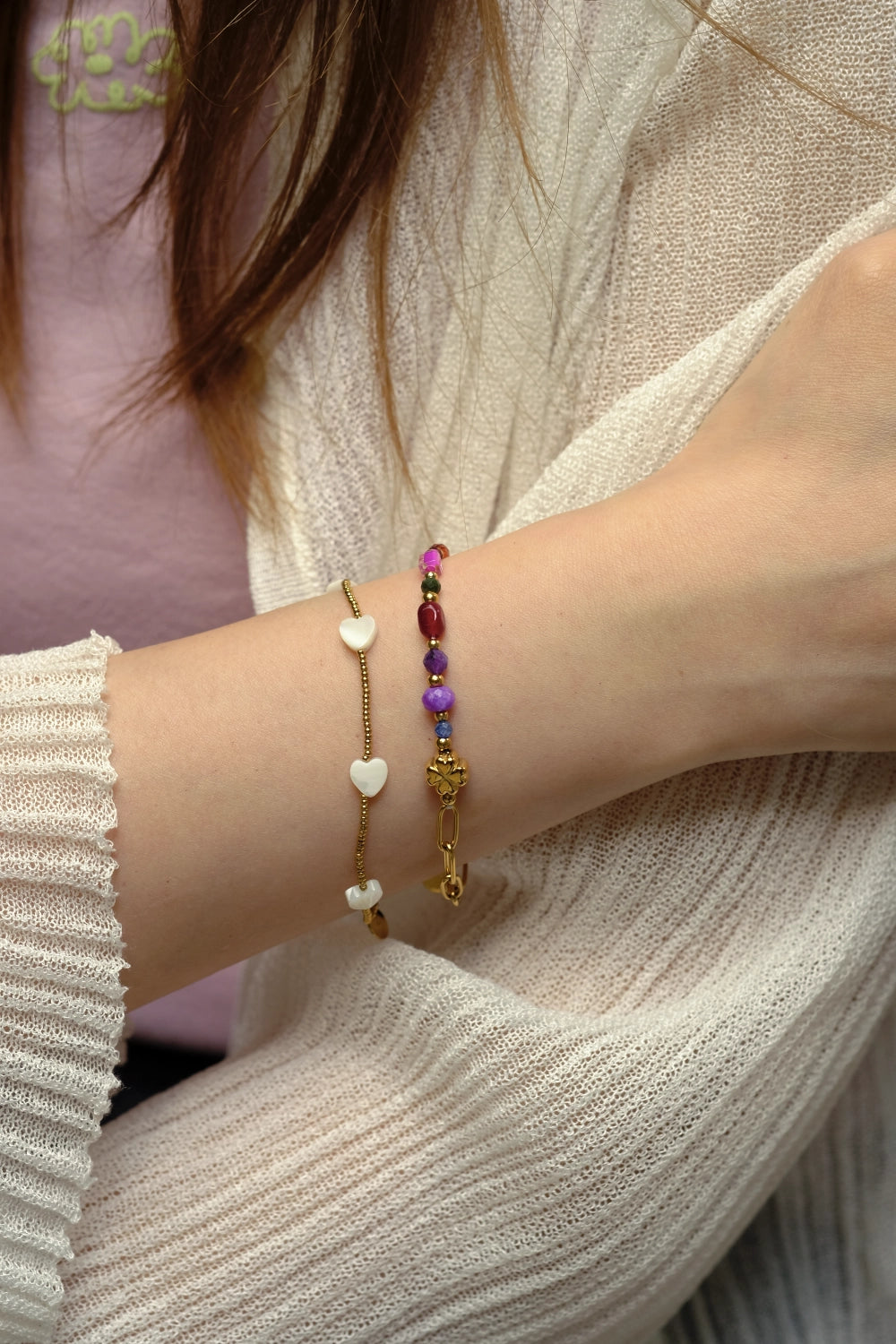 Close-up of a wrist wearing two bracelets with heart and gold designs.