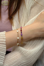 Close-up of a wrist wearing two bracelets with heart and gold designs.