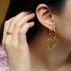 Close-up of a person wearing gold heart-shaped earrings with a blurred background.