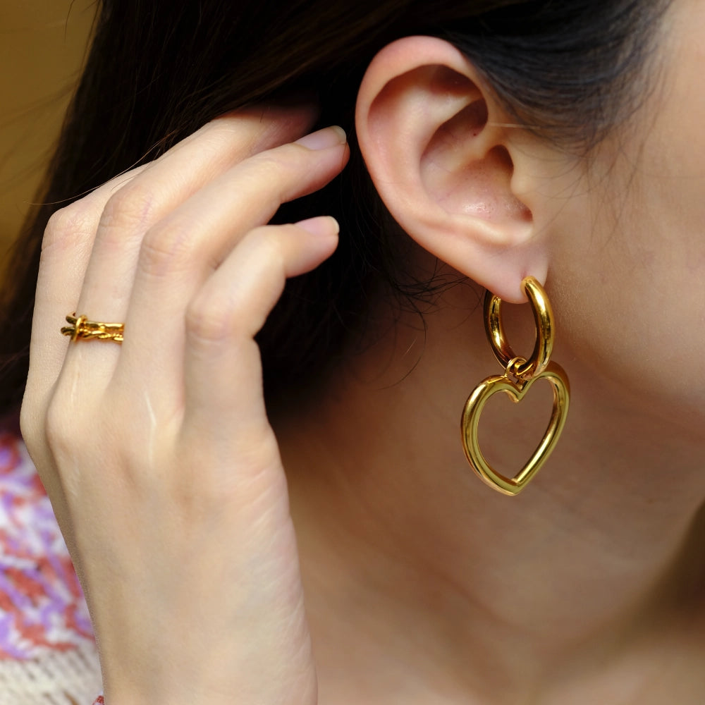 Close-up of a person wearing gold heart-shaped earrings with a blurred background.
