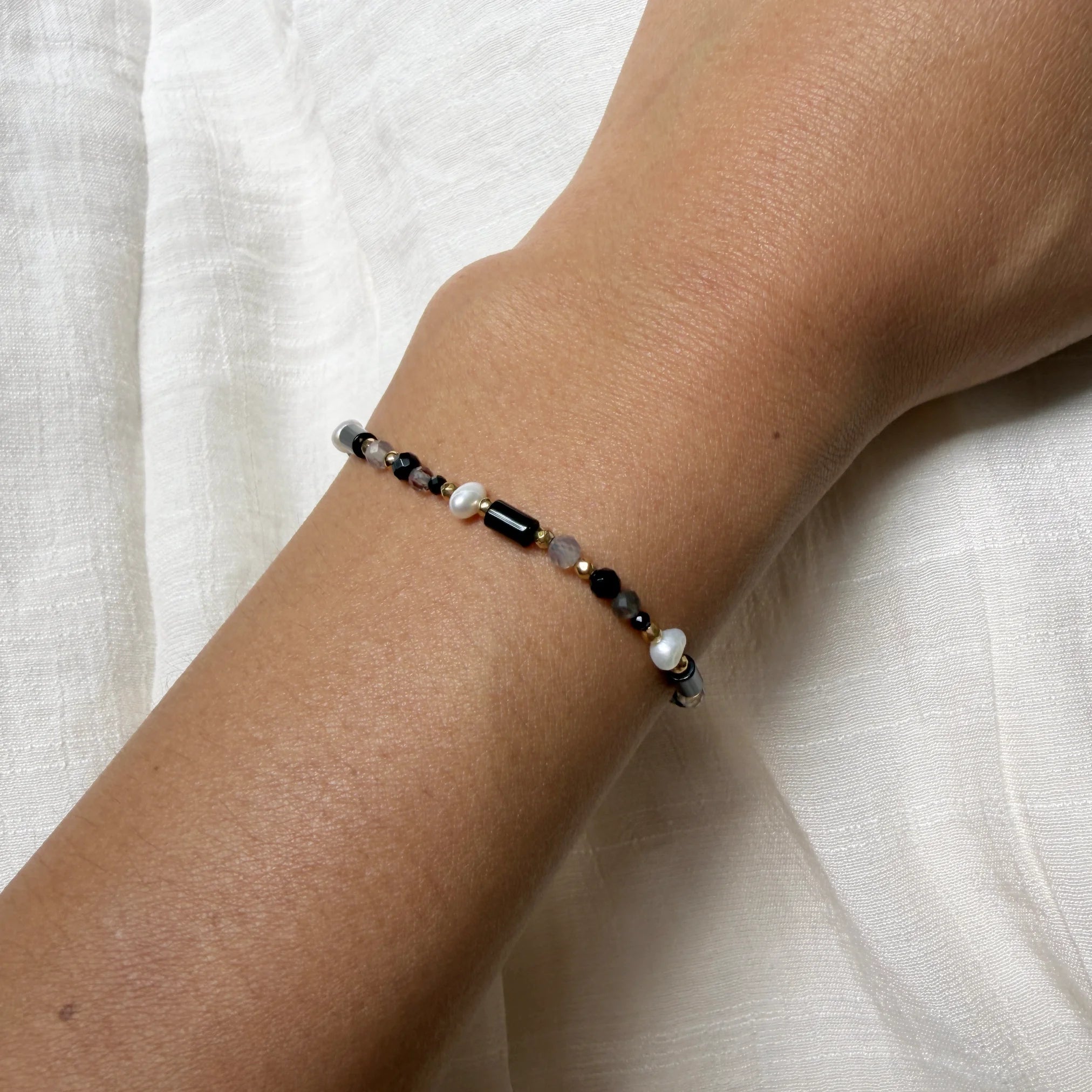 Bracelet with black and white beads on a wrist against a white fabric background