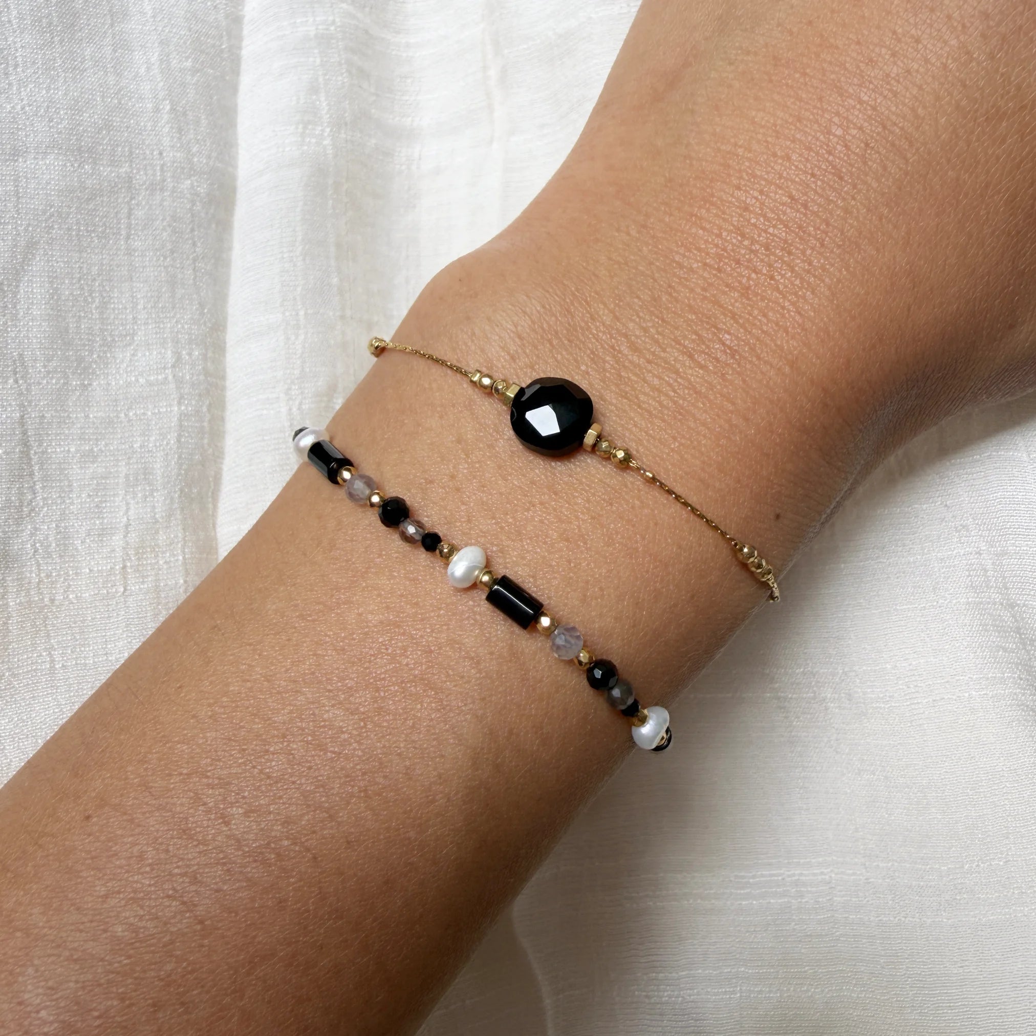 Bracelet with black stone and pearls on a wrist against a white background
