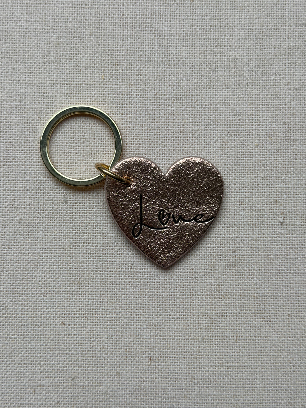 Heart-shaped keychain with 'Love' engraving on a textured gray background