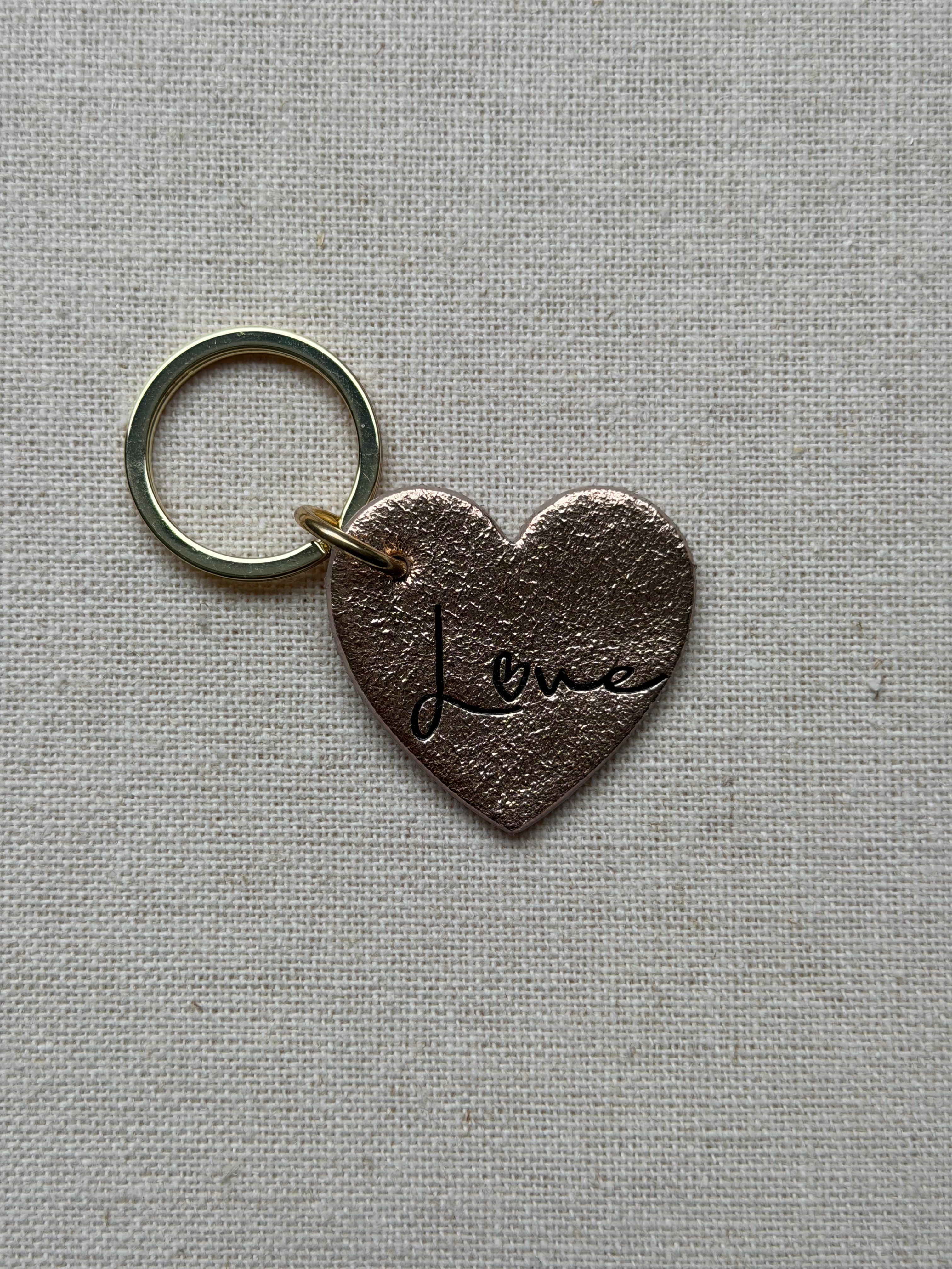 Heart-shaped keychain with 'Love' engraving on a textured gray background
