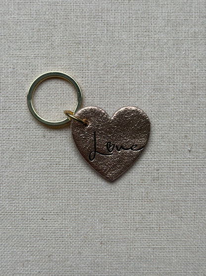 Heart-shaped keychain with 'Love' engraving on a textured gray background