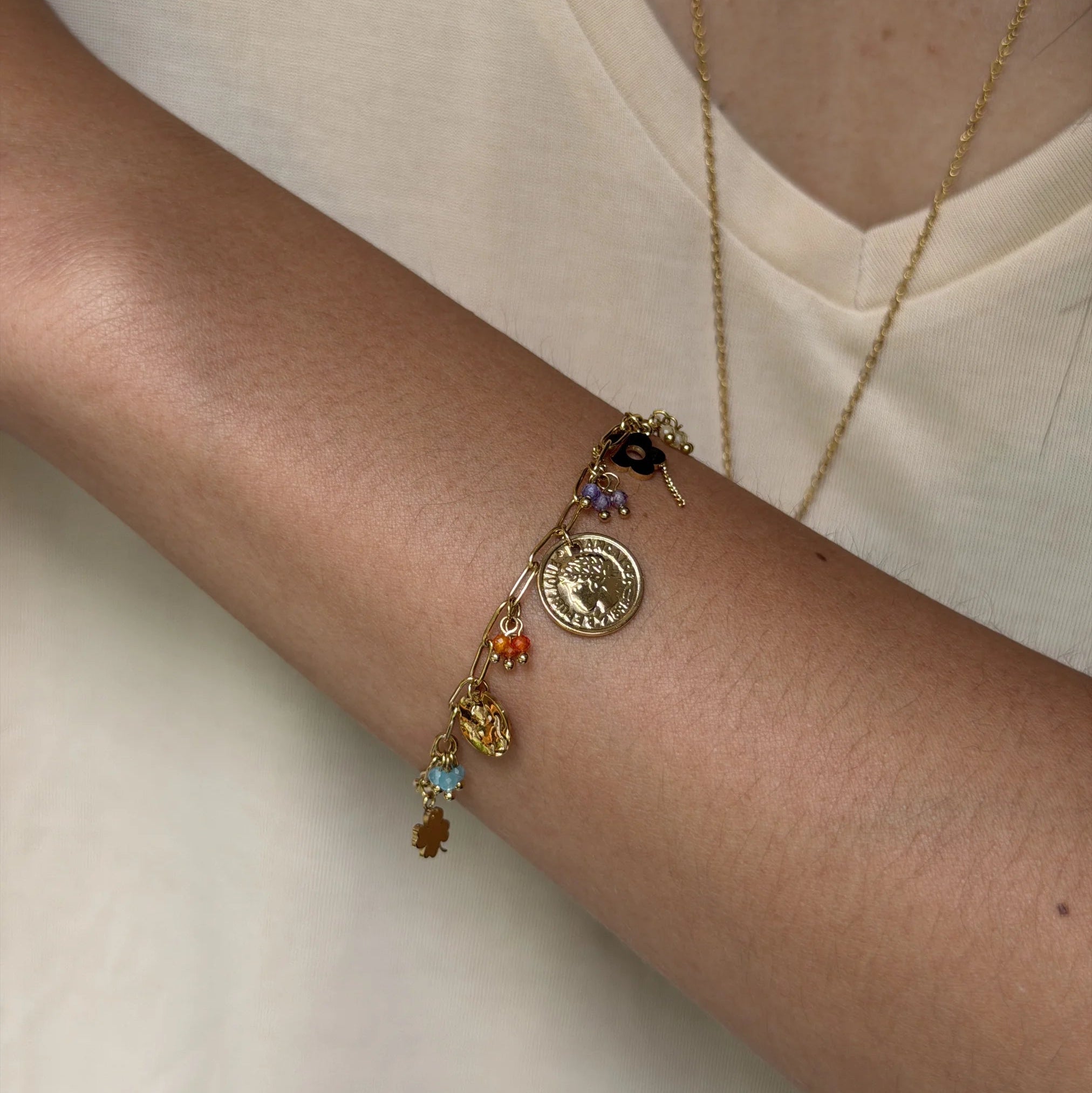 Gold bracelet with colorful charms on a wrist against a neutral background