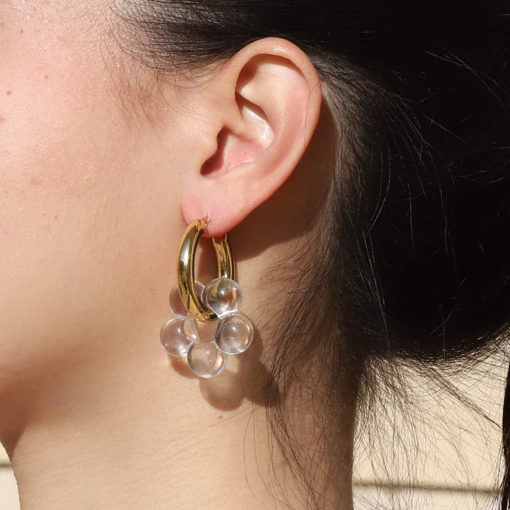 Close-up of an ear wearing a gold hoop earring with clear resin flower.