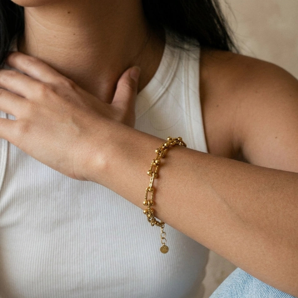 Close-up of a person wearing a gold bracelet on a neutral background