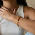 Close-up of a person wearing a gold bracelet on a neutral background