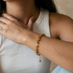 Close-up of a person wearing a gold bracelet on a neutral background