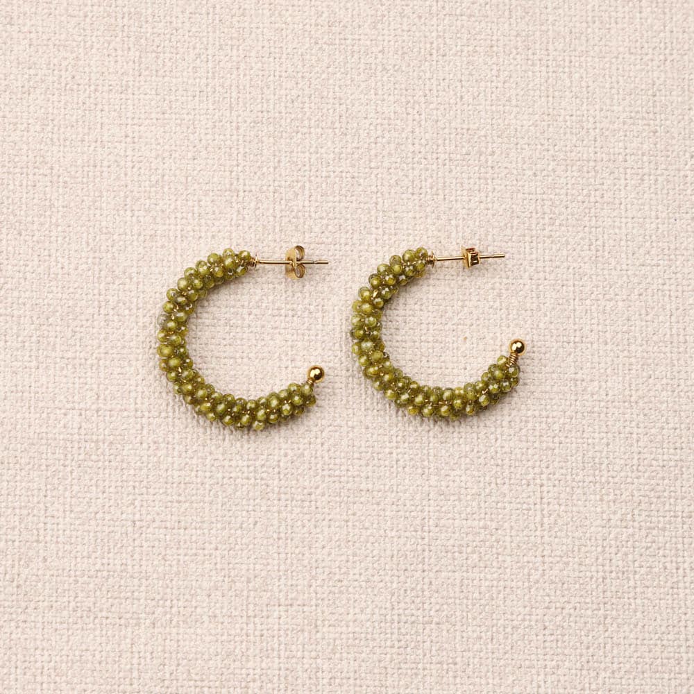 Pair of green beaded hoop earrings on a beige fabric background