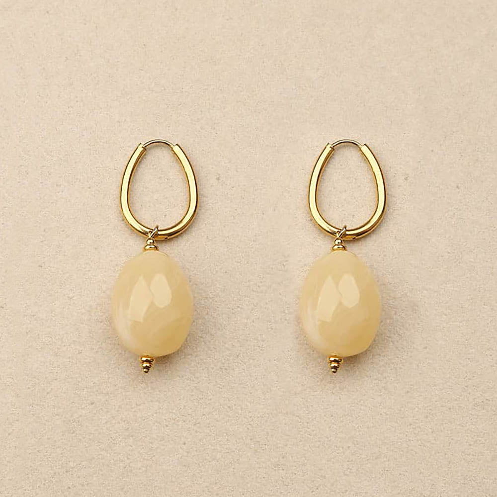 Pair of gold hoop earrings with beige teardrop-shaped beads on a beige background