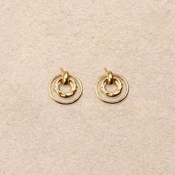 Pair of gold earrings on a beige fabric background