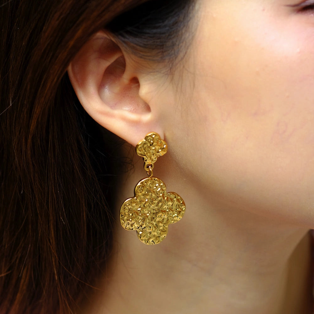 Gold floral earrings worn by a person with brown hair.