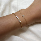 Gold bracelet with pearl beads on a wrist against a white fabric background