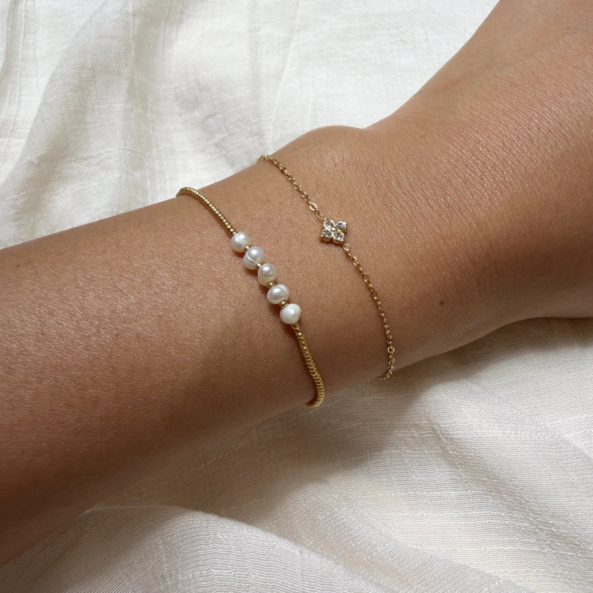 Gold bracelet with pearl beads on a wrist against a white fabric background