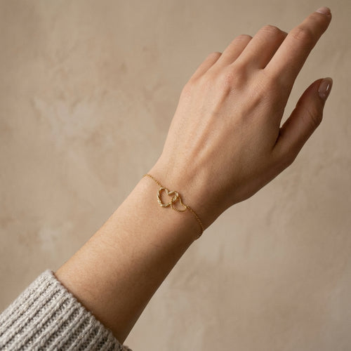 Hand wearing a gold bracelet on a beige background