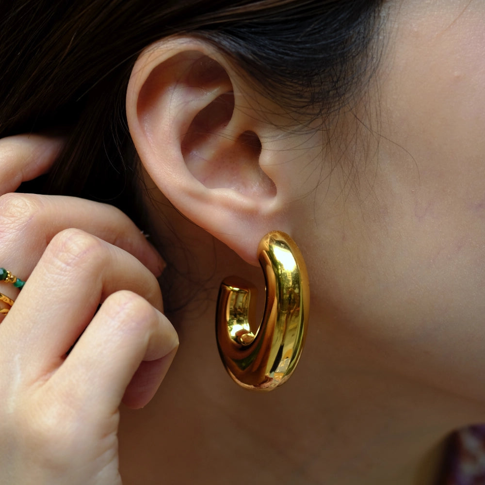 Gold hoop earring being worn on an ear with a blurred background