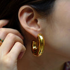 Gold hoop earring being worn on an ear with a blurred background
