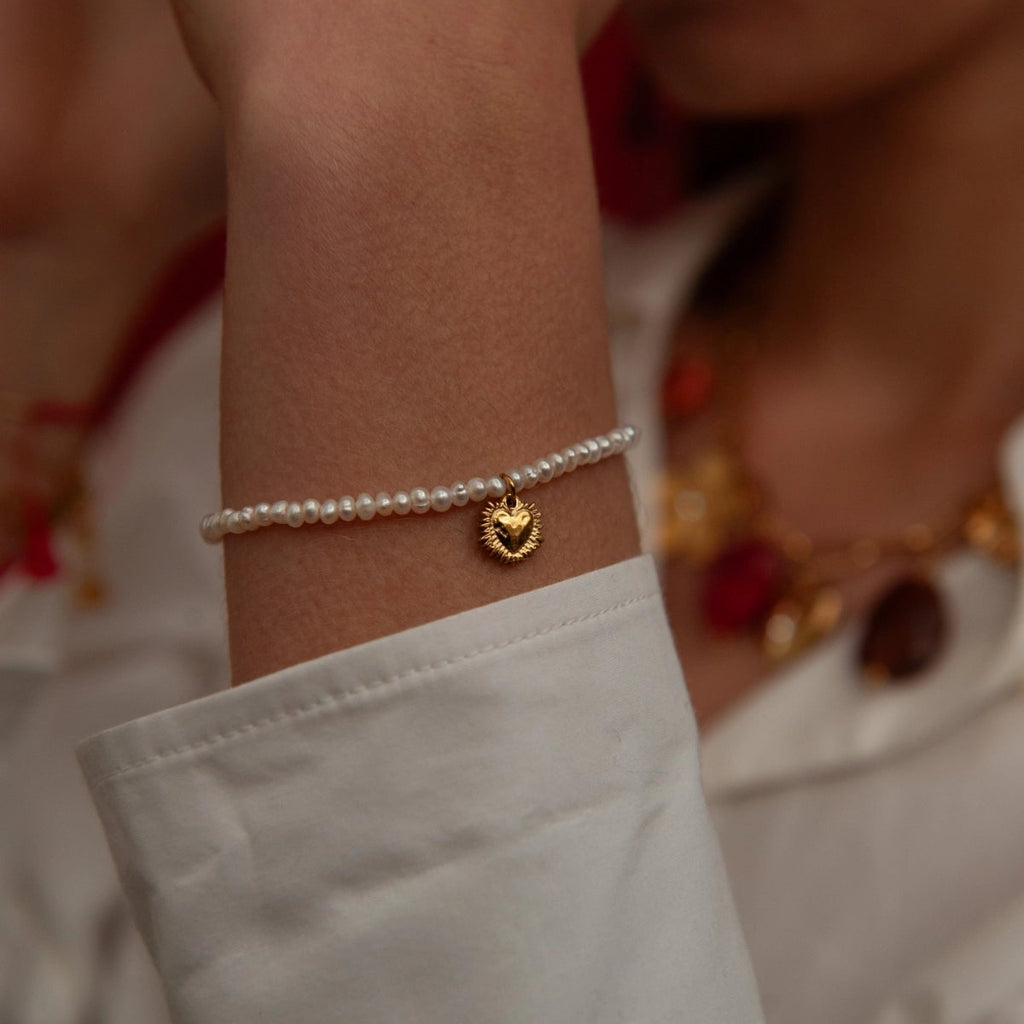 Close-up of a wrist wearing a pearl bracelet with a gold heart charm, blurred background