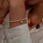 Close-up of a wrist wearing a pearl bracelet with a gold heart charm, blurred background