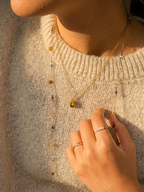 Close-up of a person wearing a beige sweater with a necklace and ring.