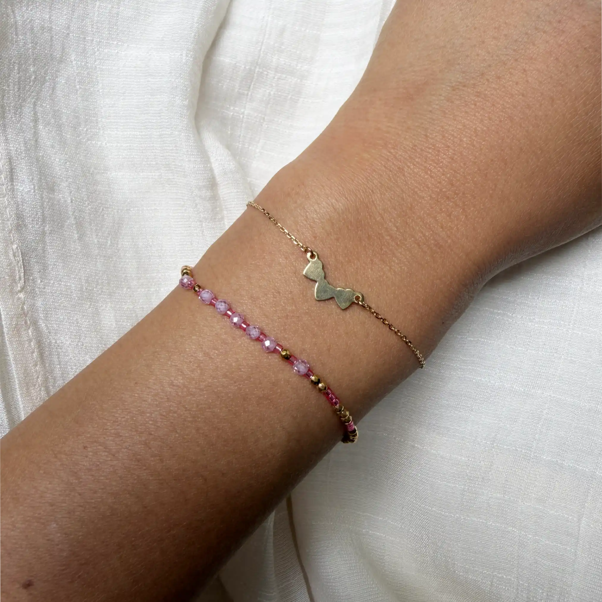 Two delicate bracelets on a wrist against a white background