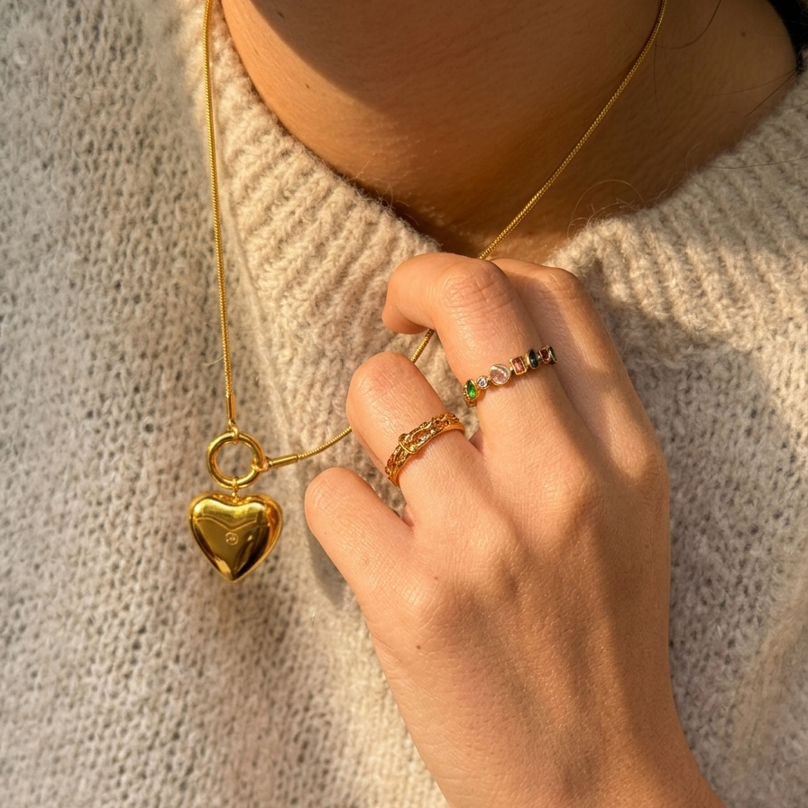 Hand wearing a gold ring with a heart pendant on a textured surface